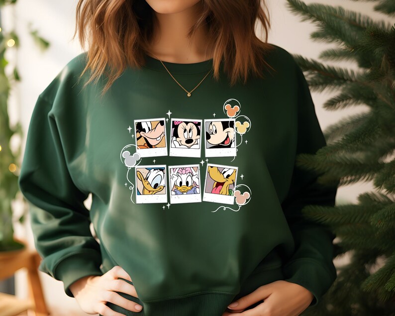 May include: A dark green sweatshirt with a graphic print of Mickey Mouse and friends in photo frames. The print includes Mickey Mouse, Minnie Mouse, Donald Duck, Goofy, and Pluto.