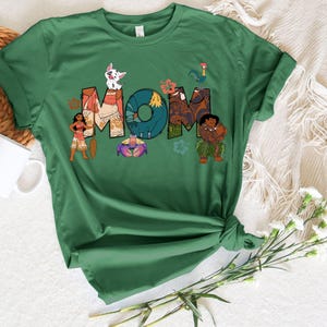 May include: Green t-shirt featuring a graphic of characters from the film Moana spelling out the word "MOM".