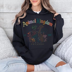 May include: Black hooded sweatshirt with the text "Animal Kingdom" in colorful lettering. The design includes a giraffe and other animal illustrations, with "Orlando" and "1998" printed below. The sweatshirt has a front pocket.