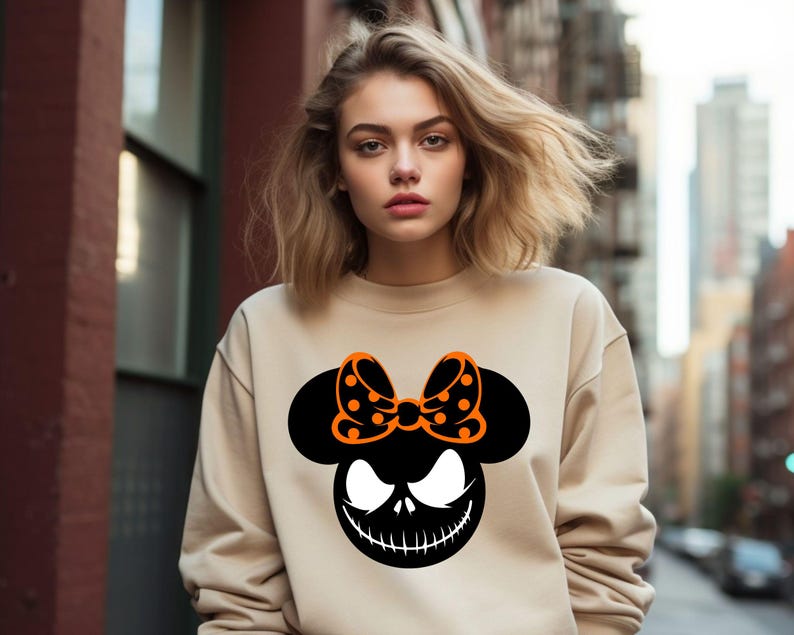 Puede incluir: Sudadera beige con un gr&aacute;fico negro y naranja. El gr&aacute;fico combina una silueta de Mickey Mouse con una cara de Jack Skellington y un lazo de lunares. Es una prenda informal de manga larga.