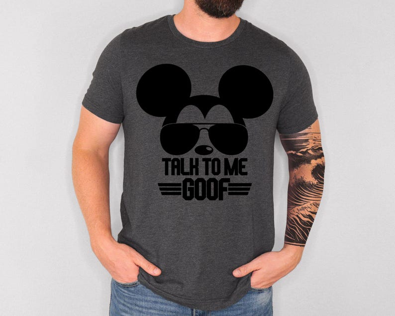 May include: A dark heather gray short-sleeve t-shirt featuring a black graphic of a mouse silhouette wearing sunglasses. Below the graphic, the text reads "TALK TO ME GOOF" in bold black capital letters, flanked by two horizontal black lines.