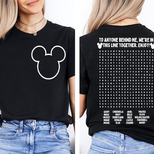 K&ouml;nnte beinhalten: Schwarzes T-Shirt mit wei&szlig;em Mickey Mouse-Umriss auf der Vorderseite. Auf der R&uuml;ckseite steht der Text "TO ANYONE BEHIND ME, WE'RE IN THIS LINE TOGETHER. ENJOY!" und ein Disney-Wortsuchr&auml;tsel.