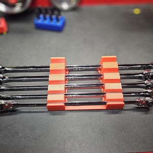 May include: A set of black and silver ratcheting wrenches, neatly organized in a red and orange holder. The wrenches are labeled with size measurements. The background includes additional tool organizers.