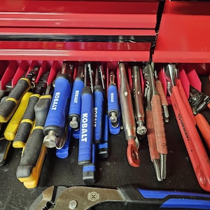 May include: A red toolbox drawer filled with various tools, including pliers, screwdrivers, and wrenches. The tools are organized in a row and labeled with the brand name "Kobalt".