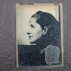 May include: Black and white photo of actress Norma Shearer, wearing a hat and looking to the side. The photo is from 1934 and is part of a magazine article about her role in the film "Riptide".
