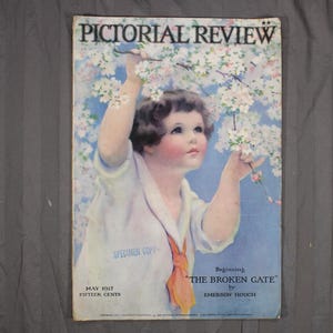 May include: A vintage magazine cover titled "PICTORIAL REVIEW" featuring a child reaching for flowering branches. The cover art has a soft, pastel color palette with text that reads "Beginning THE BROKEN GATE by EMERSON HOUGH". The magazine is dated May 1917.