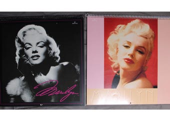 May include: Two vintage calendars featuring black and white and color photos of Marilyn Monroe. The calendars have a pink background and the word "Marilyn" printed in white.