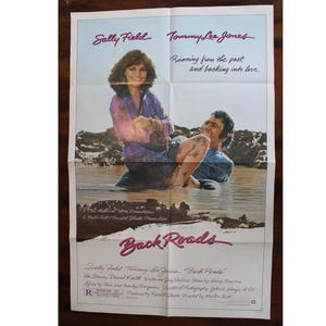 May include: Movie poster for the film "Back Roads" starring Sally Field and Tommy Lee Jones. The poster features a photo of the two actors in a river, with the title of the film in large, pink letters.