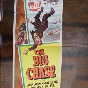 May include: Vintage movie poster for "The Big Chase." The poster features a man falling from a helicopter, with the words "RAW! ROUGH! VIOLENT!" at the top. The title is in large orange letters.