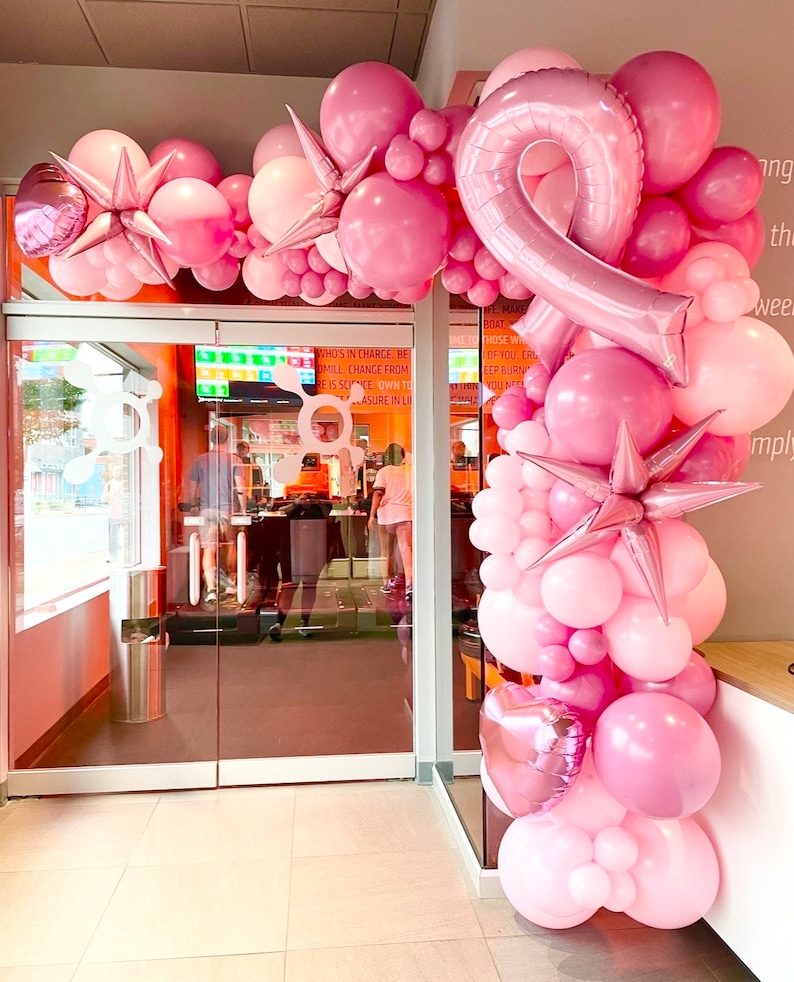 Peut inclure: Une arche de ballons rose et blanche avec un grand ballon en forme de ruban rose au centre. L'arche est d&eacute;cor&eacute;e de ballons en forme d'&eacute;toile.