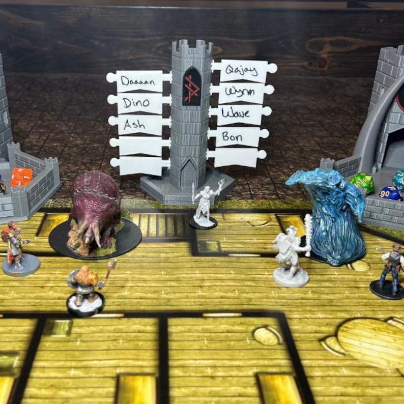 Pu&ograve; includere: Un'impostazione di gioco di ruolo da tavolo con un tabellone di gioco in legno, figure in miniatura e una struttura grigia a forma di castello con targhette. Sono presenti anche una figura di mostro viola e un elemento d'acqua blu. Dadi e altri elementi di gioco sono visibili.