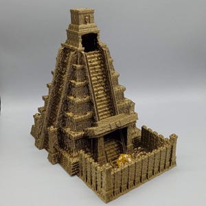 May include: A detailed, tan-colored 3D-printed dice tower in the shape of an ancient temple. The tower features multiple levels with stairs, a central opening, and a surrounding wall. A yellow and orange die rests inside the tower.