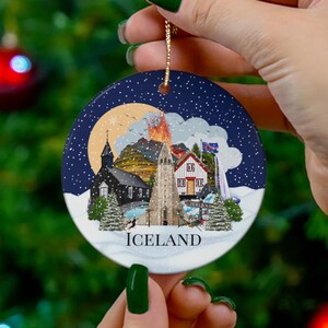 Colourful ceramic Iceland ornament with a blue background and white snow. The baubles feature a colourful illustration of popular Icelandic Landmarks like the Reykjavik church, waterfall, volcano, black sand beach, elephant rock, puffins and more! The text "ICELAND" is printed on under the design.