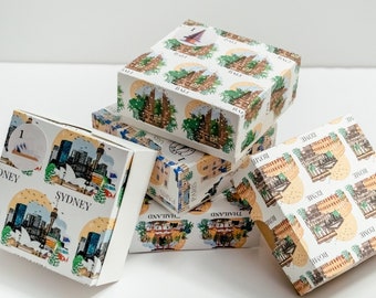 May include: Several white square boxes with travel-themed illustrations are stacked. The boxes feature images of landmarks and cityscapes, including Sydney, Rome, Bali, Paris, and Thailand. The boxes are decorated with colorful designs.