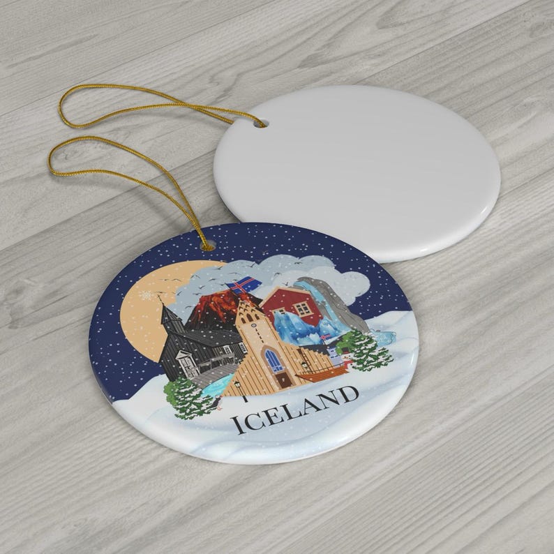 May include: Two round ceramic ornaments with gold hanging strings. One is plain white, while the other features a colorful illustration of an Icelandic landscape with a church, red house, mountains, and the text ICELAND printed in black.