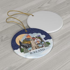 Colourful Single sided Iceland ornament with a blue background and white snow. The baubles feature a colourful illustration of popular Icelandic Landmarks like the Reykjavik church, waterfall, volcano, black sand beach, elephant rock, puffins and more! The text "ICELAND" is printed on under the design.