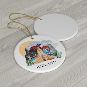 May include: Two round white ceramic ornaments with gold hanging strings. One ornament is blank, while the other features a colorful illustration of Icelandic landmarks, including a church and mountains, with the text ICELAND printed below.