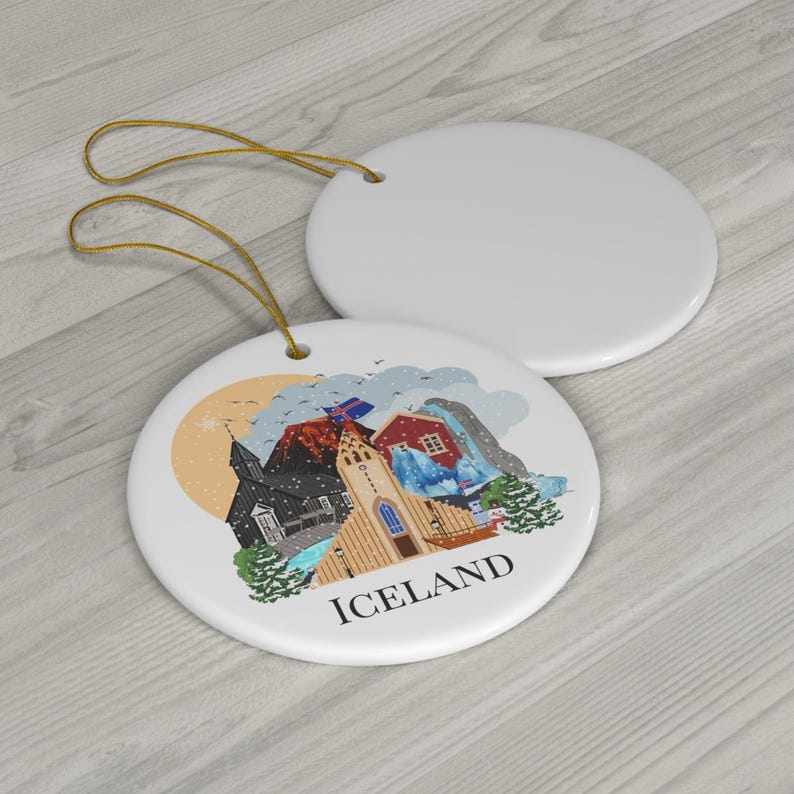 May include: Two round white ceramic ornaments with gold hanging strings. One ornament is blank, while the other features a colorful illustration of Icelandic landmarks, including a church and mountains, with the text ICELAND printed below.