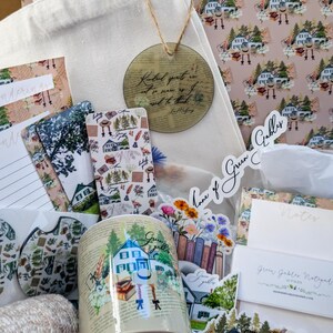 May include: A tote bag filled with Green Gables themed items, including a mug, stickers, a bookmark, and a notepad. The tote bag is white with a quote about kindness printed on it. The items are all decorated with a green and white color scheme and feature illustrations of houses, books, and flowers.