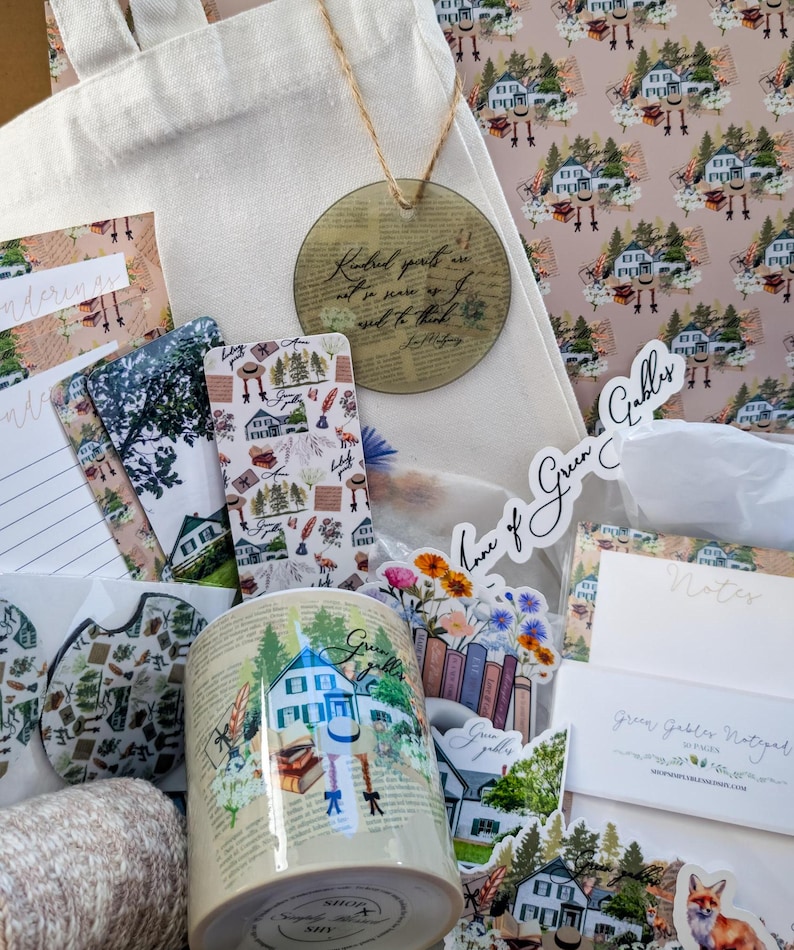 May include: A tote bag filled with Green Gables themed items, including a mug, stickers, a bookmark, and a notepad. The tote bag is white with a quote about kindness printed on it. The items are all decorated with a green and white color scheme and feature illustrations of houses, books, and flowers.