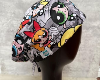 May include: A gray surgical scrub cap featuring a colorful cartoon design. The cap is patterned with images of cartoon characters in various poses. The cap has a tie in the back and a small label on the side.