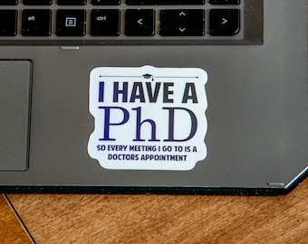 May include: A white sticker with black text that reads "I HAVE A PhD SO EVERY MEETING I GO TO IS A DOCTORS APPOINTMENT". The sticker is on a gray laptop.