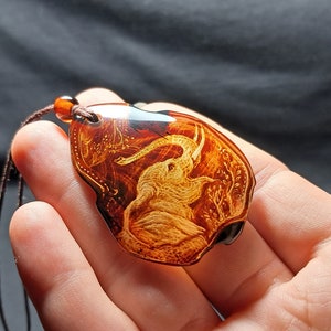 Può includere: Un ciondolo in ambra marrone con una scultura dettagliata di un elefante. Il ciondolo è su un cordoncino marrone.