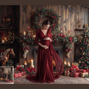May include: A pregnant woman in a long, red dress stands in front of a fireplace decorated with Christmas greenery. A Christmas tree with ornaments is in the background.