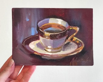 May include: Oil painting of a teacup and saucer. The cup and saucer are white with gold trim. The cup is filled with a dark liquid, likely coffee or tea. The background is a dark maroon color.
