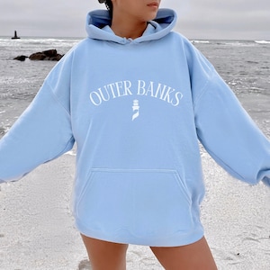 May include: A light blue hoodie with a white graphic of a lighthouse and the text "OUTER BANKS" in a curved arc.