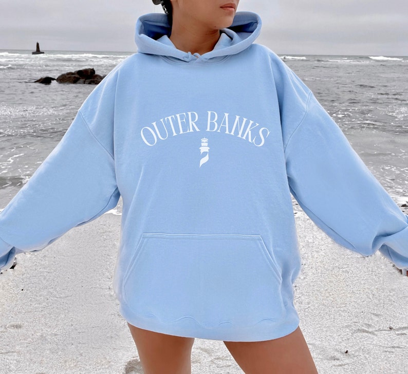 May include: A light blue hoodie with a white graphic of a lighthouse and the text "OUTER BANKS" in a curved arc.