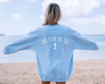 May include: A light blue sweatshirt with the text "HILTON HEAD" arched across the back in white. Below the text is a white lighthouse graphic. The sweatshirt is a solid light blue color.