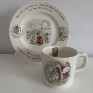以下が含まれることがあります： ビートリックス・ポターのイラストが描かれた白い陶器のティーカップとソーサーのセット。ソーサーには「Once upon a time there was a little girl called Lucie, who lived at a farm called Little-town.」というテキストが書かれています。ティーカップには「She was a good girl, only she was always losing her way.」というテキストが書かれています。