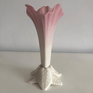 Puede incluir: Un jarrón de cerámica con una parte superior en forma de trompeta en un degradado de rosa a blanco. La base es un diseño estilizado en forma de estrella. El jarrón es un artículo decorativo.