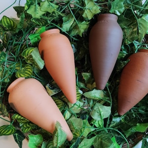 Peut inclure: Quatre vases en terre cuite de forme amphore sont disposés sur un lit de feuilles artificielles vertes et jaunes. Les vases varient en couleur, du beige clair au brun foncé.