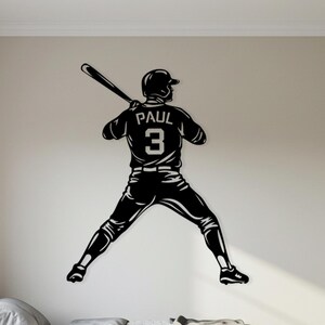 Może przedstawiać: Czarna grafika ścienna przedstawiająca sylwetkę baseballisty w pozycji do odbicia. Na koszulce zawodnika widnieje imię "PAUL" i numer "3". Grafika jest zamontowana na ścianie w neutralnym kolorze nad łóżkiem.