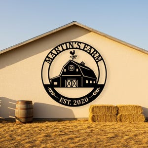 May include: Black metal farm sign with the text "MARTIN'S FARM" in a circular design, featuring a barn silhouette and a rooster weathervane. The sign includes "EST. 2020" and wheat stalks. The sign is mounted on a beige wall.