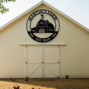 May include: Black metal sign with the text "MARTIN'S FARM" encircling a barn illustration, a rooster weathervane, and "EST. 2020". The sign is mounted on a cream-colored barn with white double doors. Chickens are in the foreground.