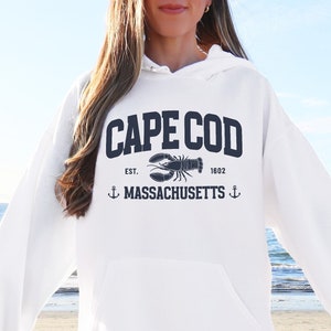May include: White hooded sweatshirt with a navy blue graphic of a lobster and the text "Cape Cod Est. 1602 Massachusetts"