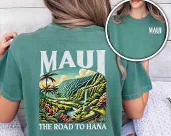 May include: A light green t-shirt featuring a graphic of a scenic road in Maui, Hawaii. The text "Maui The Road to Hana" is printed on the shirt.