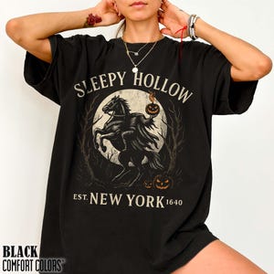 May include: Black t-shirt with a graphic featuring the Headless Horseman on horseback, a full moon, and the words "Sleepy Hollow Est. New York 1640." The shirt also has the words "Black Comfort Colors" at the bottom.