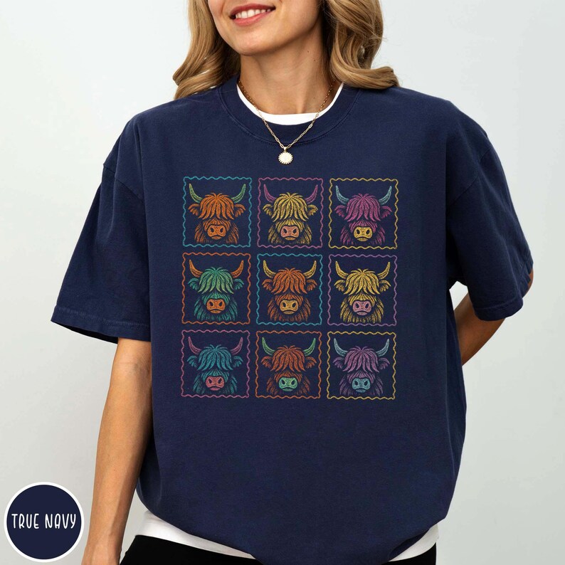 May include: Navy blue t-shirt featuring a grid of nine colorful Highland cow illustrations. Each cow is framed within a postage stamp-like border. The shirt has a relaxed fit and short sleeves. The text "TRUE NAVY" is printed on the bottom left.
