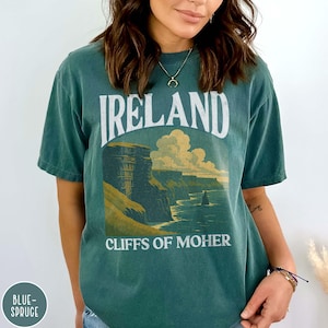 May include: Green t-shirt with the word "IRELAND" in white arched text above a scenic illustration of the Cliffs of Moher. The text "CLIFFS OF MOHER" is below the illustration. The shirt has a vintage, faded look.