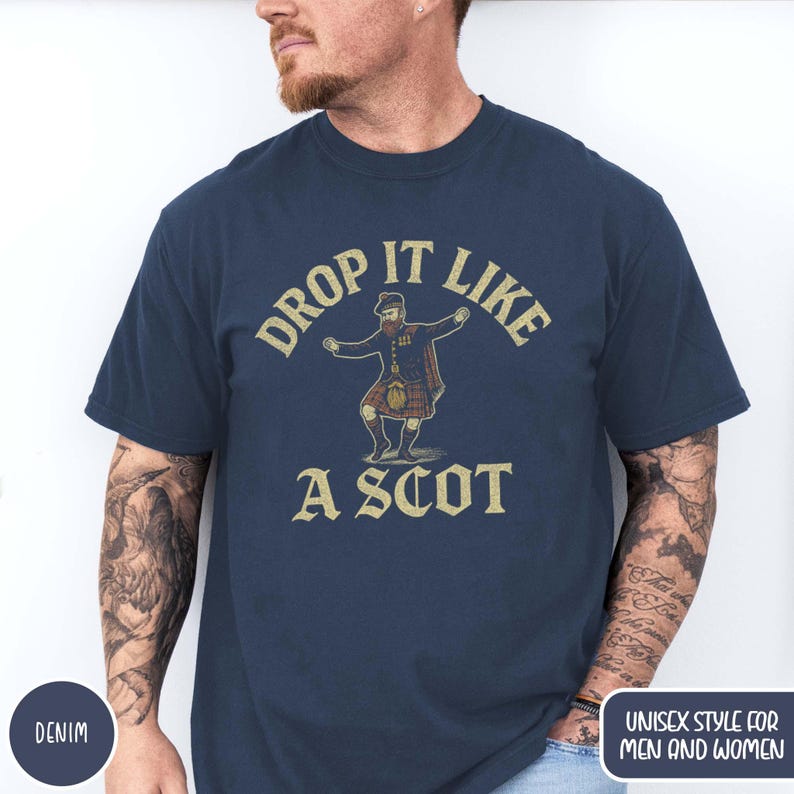 Puede incluir: Camiseta azul marino con la frase "DROP IT LIKE A SCOT" y una ilustraci&oacute;n de un hombre con kilt. El dise&ntilde;o tiene un aspecto vintage. La camiseta est&aacute; etiquetada como "DENIM" y "UNISEX STYLE FOR MEN AND WOMEN".