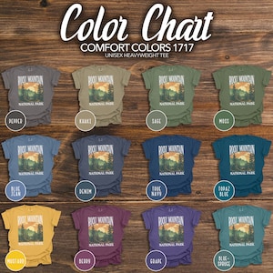May include: Color chart for unisex heavyweight t-shirts featuring a graphic of Rocky Mountain National Park in various colors, including pepper, khaki, sage, moss, blue jean, denim, true navy, topaz blue, mustard, berry, grape, and blue spruce.