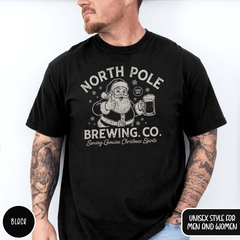 May include: Black t-shirt with a graphic featuring Santa Claus giving a thumbs up and holding a beer mug. The text reads "NORTH POLE BREWING CO. Serving Genuine Christmas Spirits" in a vintage style. The shirt is labeled "UNISEX STYLE FOR MEN AND WOMEN."