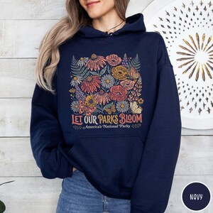 May include: Navy blue hoodie featuring a floral design with the text "Let Our Parks Bloom" and "America's National Parks." The design includes colorful flowers and the names of national parks.