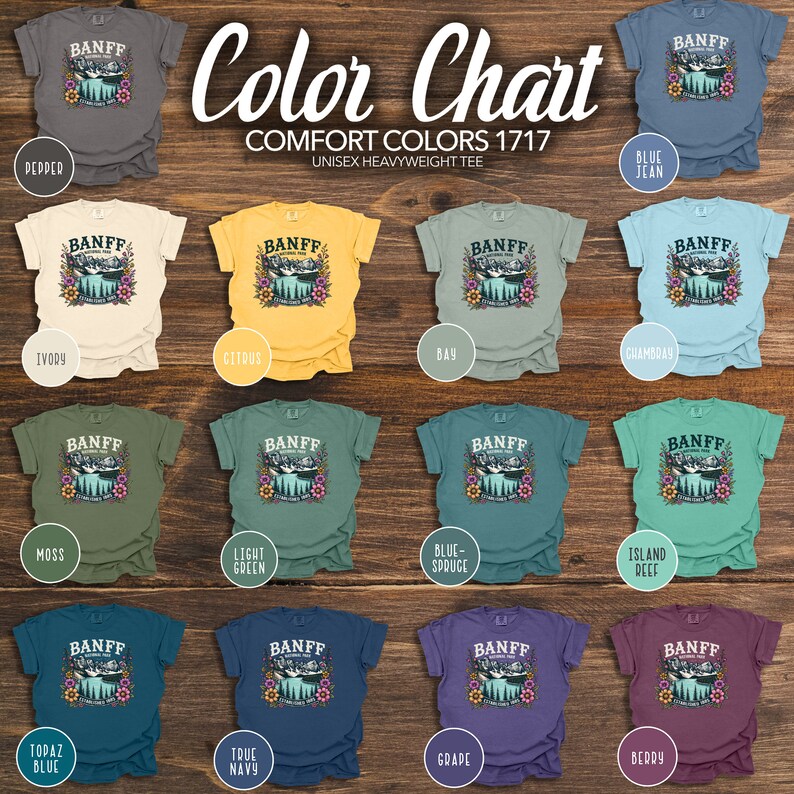 May include: Color chart showing 12 different t-shirt colors with a graphic of a lake and mountains with the word "Banff" printed on the front. The colors are: Depder, Ivory, Moss, Citrus, Bay, Chambray, Light Green, Blue-Spruce, Island Reef, Topaz Blue, True Navy, Grape, and Berry.