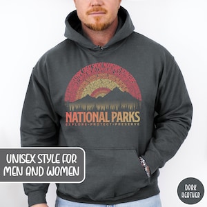 May include: Dark heather grey hooded sweatshirt with a vintage-style graphic of a mountain range with a sunset and the text "National Parks" with the words "Explore, Protect, Preserve" underneath. The graphic is surrounded by a semi-circle of text listing various national parks.