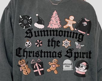 May include: Dark gray sweatshirt with the phrase "Summoning the Christmas Spirit" in gothic lettering. The design includes various Christmas-themed illustrations such as a Christmas tree, gingerbread man, and a snow globe.